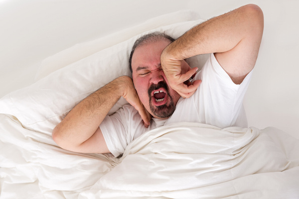 Tired man lying in bed stretching and yawning in an effort to wake up as he debates just turning over and going back to sleep in the morning