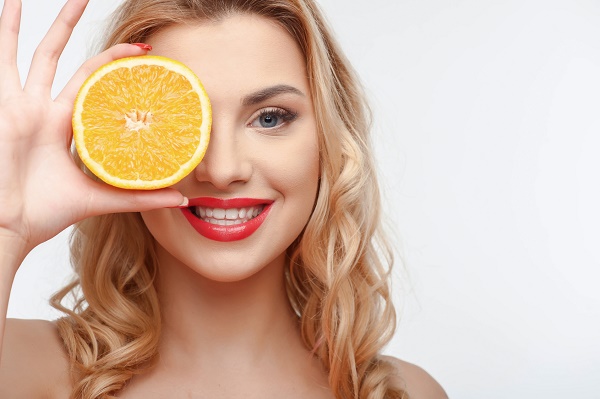 Cheerful girl is covering her eye with orange. She is smiling with enjoyment. Isolated on background and there is copy space in right side