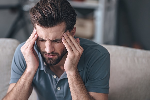 Feeling stressed. Frustrated handsome young man touching his head and keeping eyes closed while sitting on the couch at home