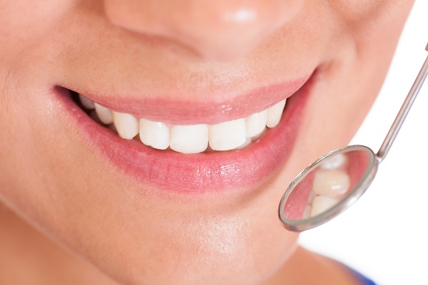 Smiling woman with perfect white teeth and a small dentists mirror reflecting her teeth being held alongside