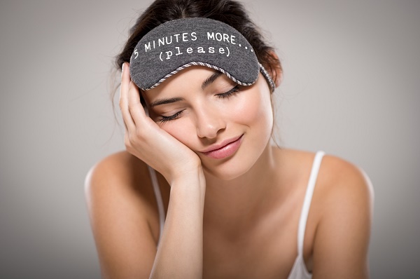Young beautiful woman sleeping with eye mask on grey background. Portrait of brunette tired girl with eye mask for sleeping. Sleepy beauty woman resting on hand with closed eyes.