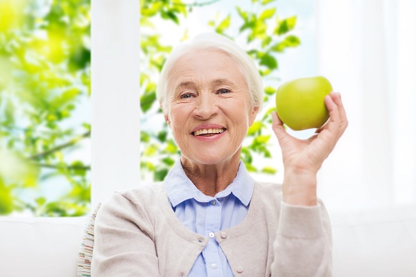 age, healthy eating and people concept - happy smiling senior woman with green apple at home over window and green natural background