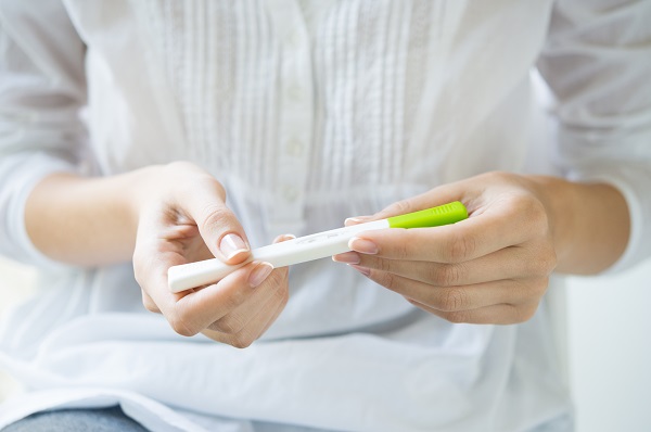 Closeup shot of a woman looking at pregnancy test. She's is checking her pregnancy exam. Detail hands of a girl holding pregnancy test. Shallow depth of field with focus on pregnancy test.
