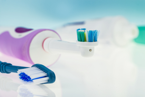 Electric and classic toothbrush on reflective surface and light blue background.