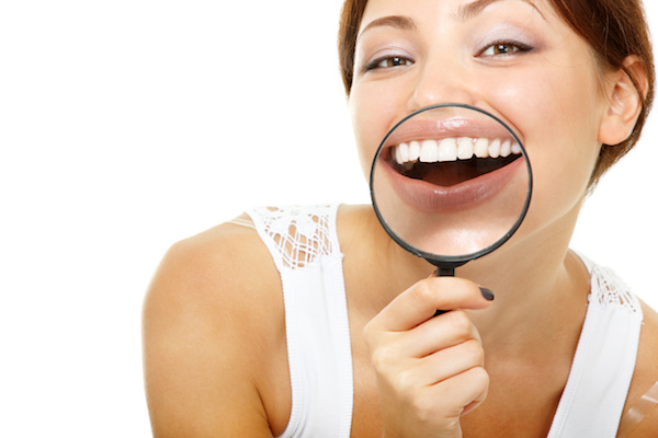 funny woman smiling and show teeth through a magnifying glass over white background