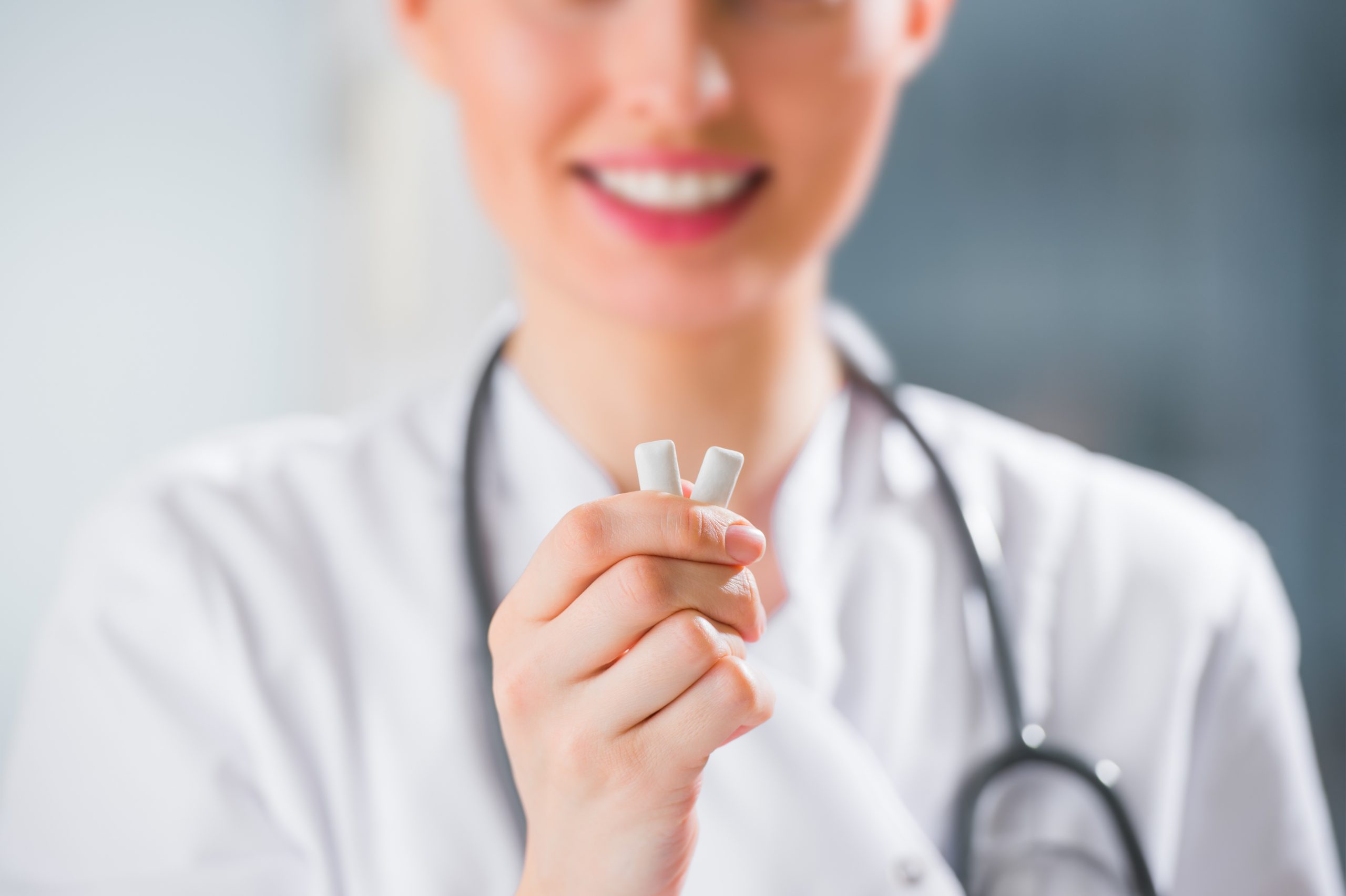 Young female dentist doctor holding chewing gum and smiling. Oral hygiene concept