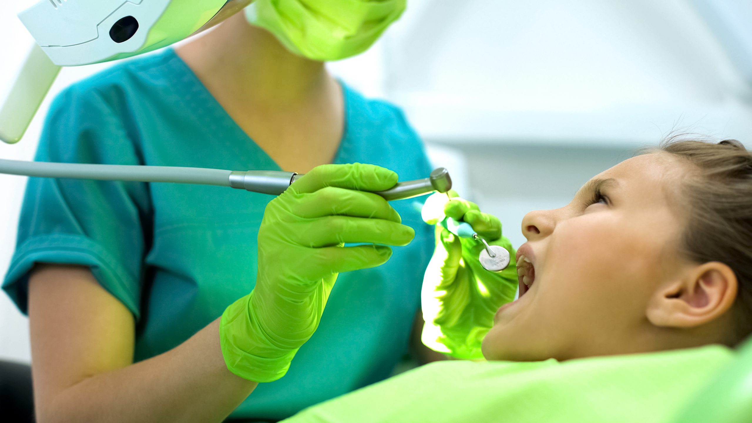 Little girl sitting in dentist chair, letting to cure her cavities in her teeth.