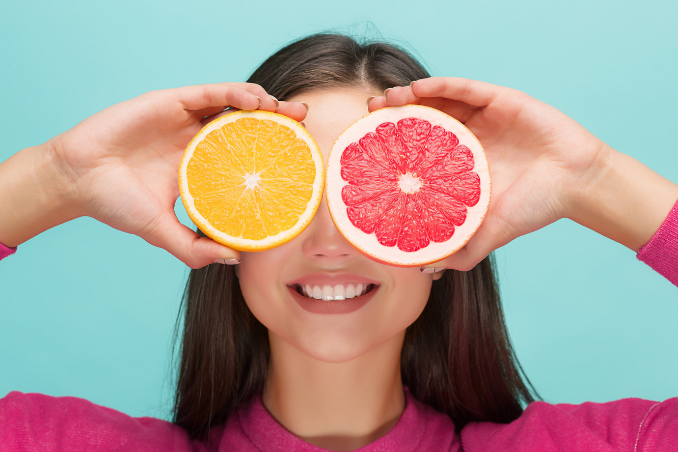 Beautiful woman's face with delicious orange and grapefruit at studio