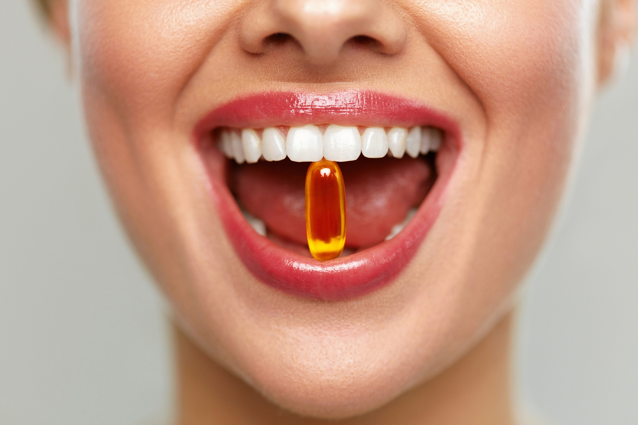 Vitamins And Food Supplements. Close Up Of Beautiful Woman Opened Mouth Holding Fish Oil Pill In White Teeth. Smiling Girl Holding Capsule With Omega-3 Between Teeth. Healthy Diet Nutrition Concept