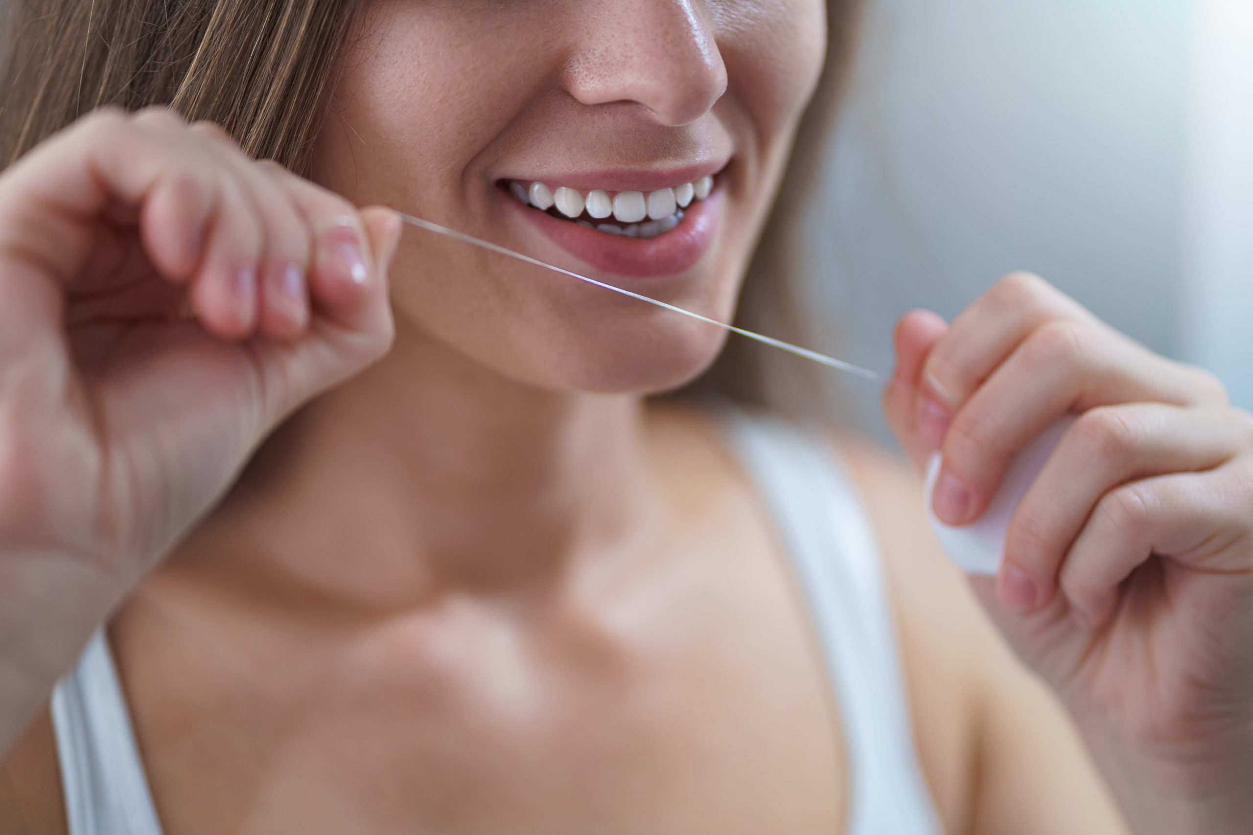 Happy healthy woman uses dental floss for brushing teeth and oral hygiene at home. Teeth oral care