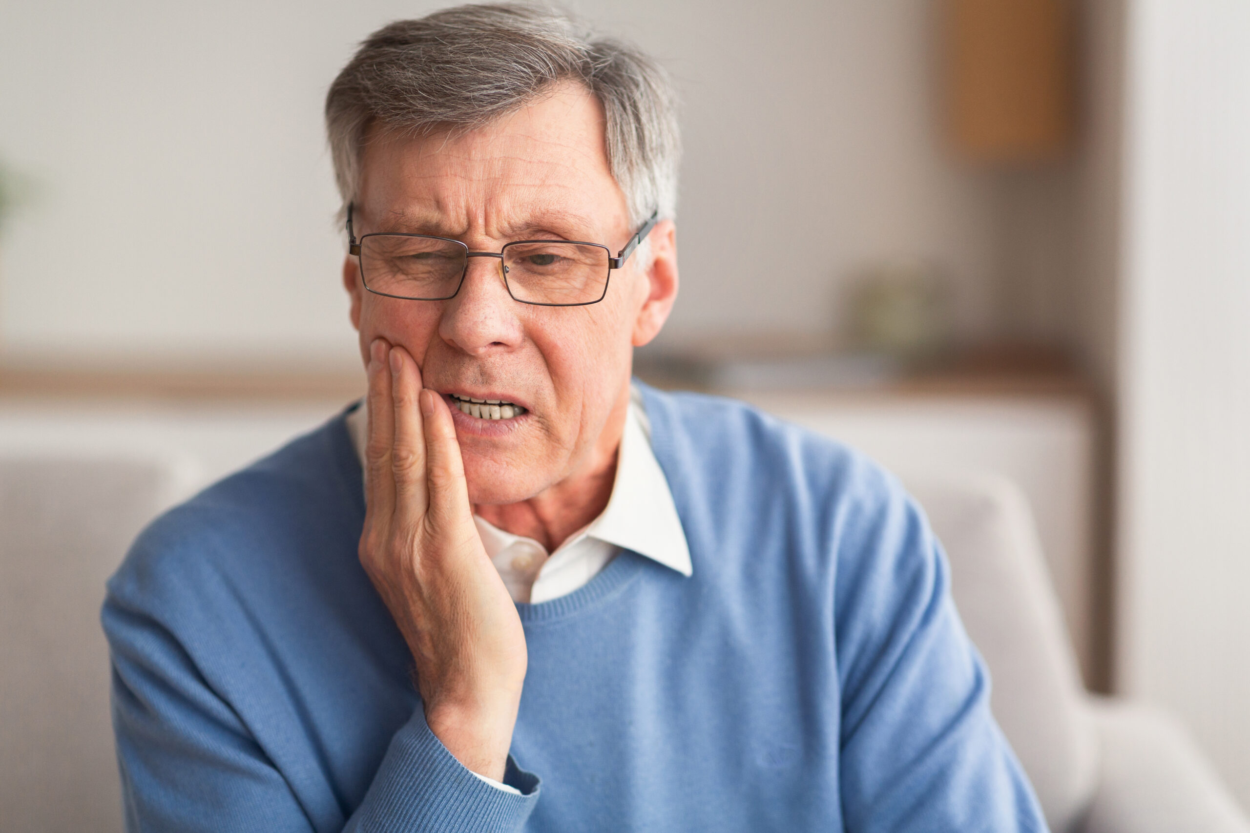 Tooth sensitivity is a common dental complaint that involves pain or discomfort in teeth when exposed to certain temperatures or substances.
Elderly Man Having Toothache Touching Cheek Suffering From Pain Sitting On Sofa At Home. Selective Focus