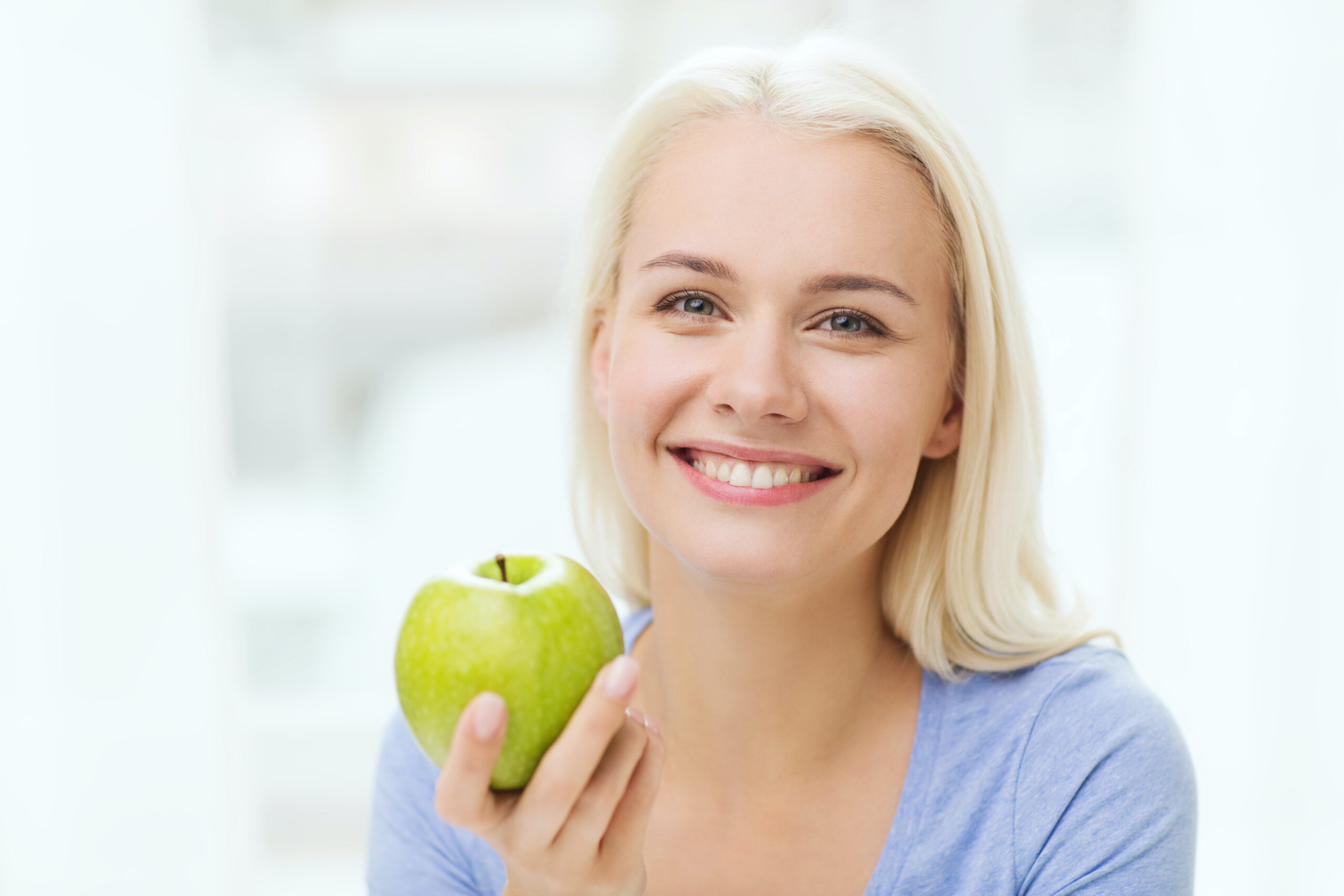 healthy eating, organic food, fruits, diet and people concept - happy woman eating green apple at home