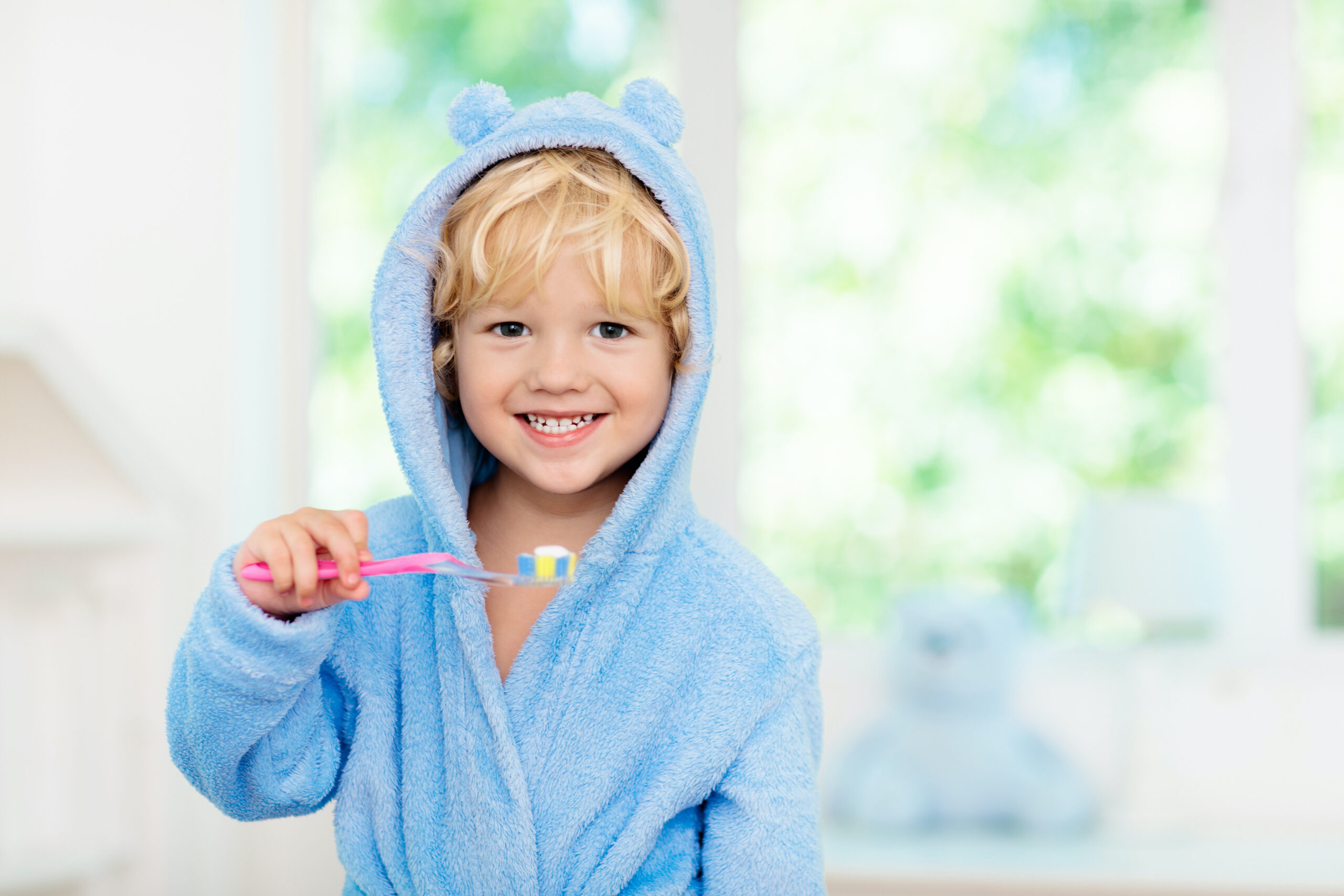 Child brushing teeth. Kids tooth brush and paste. Little baby boy in blue bath robe or towel brushing his teeth in white bathroom with window on sunny morning. Dental hygiene and heath for children. fluoride services