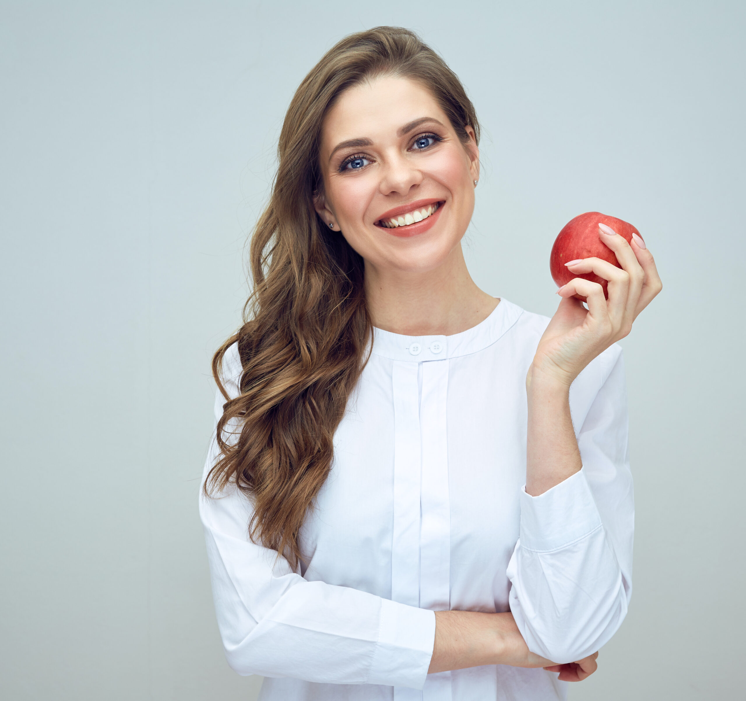 woman with toothy smile wearing white shirt holding red apple. isolated studio portrait.
diet and teeth