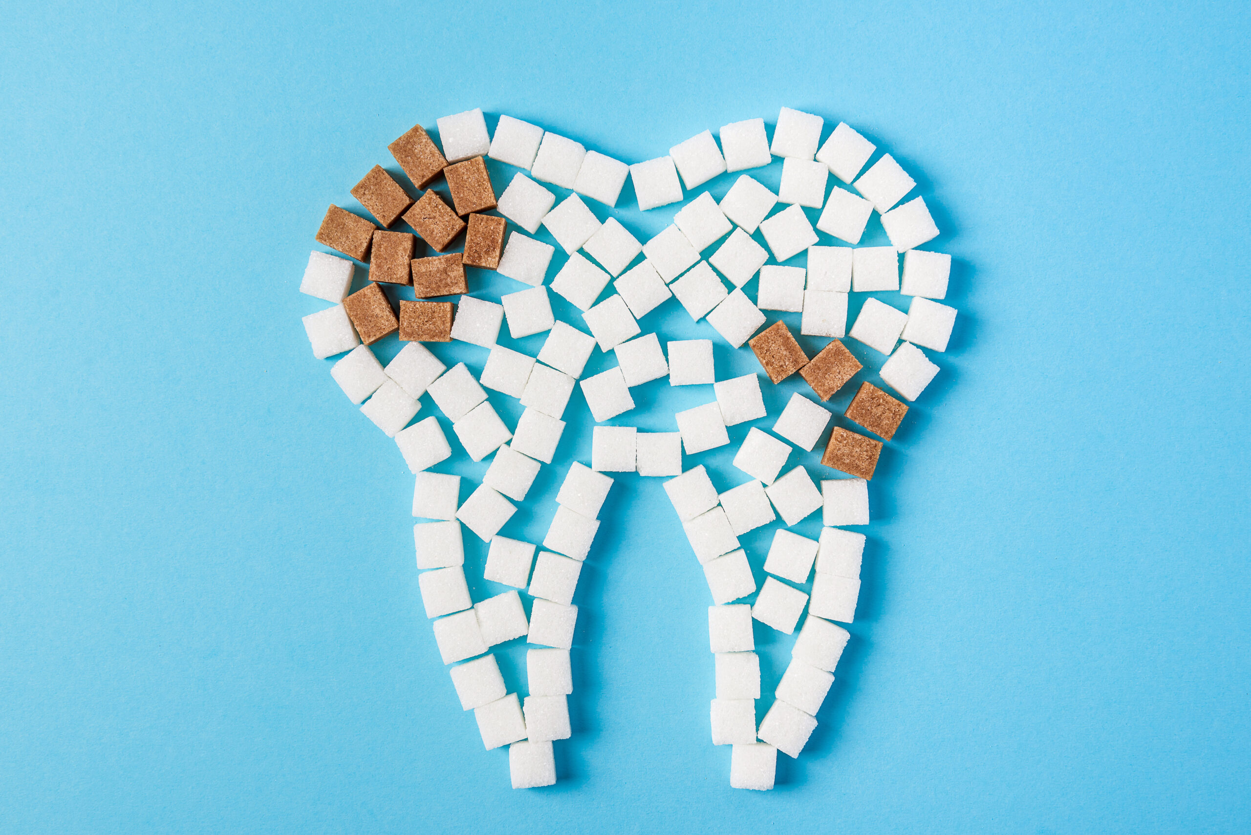 Sugar destroys the tooth enamel and leads to tooth decay. Tooth made of white sugar cubes and caries made of brown sugar cubes. Top view. Close up