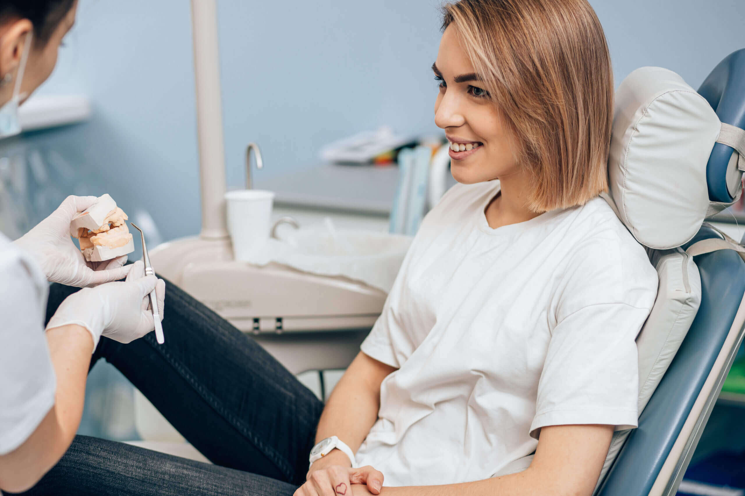 early dental treatment friendly doctor dentist examine teeth of caucasian young woman in casual wear, isolated in dentist office, using special medical equipment