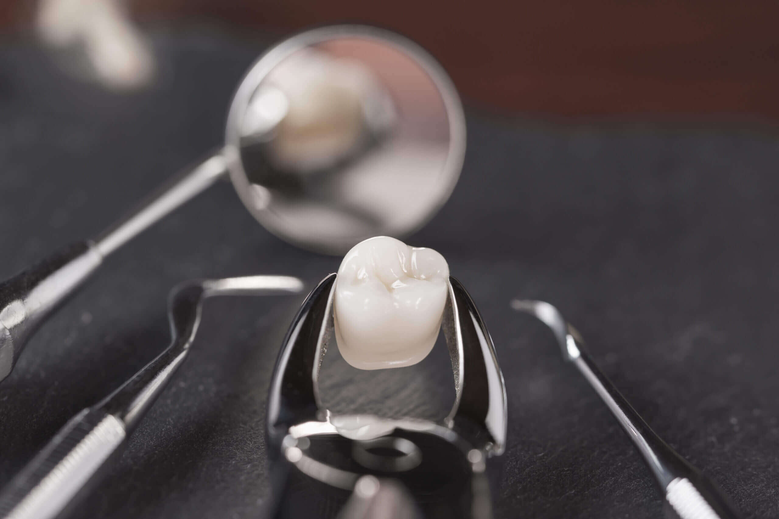 Tooth extraction concept with an array of stainless steel dental tools and a mask with the extracted tooth clasped in the pincers and reflected in the mirror