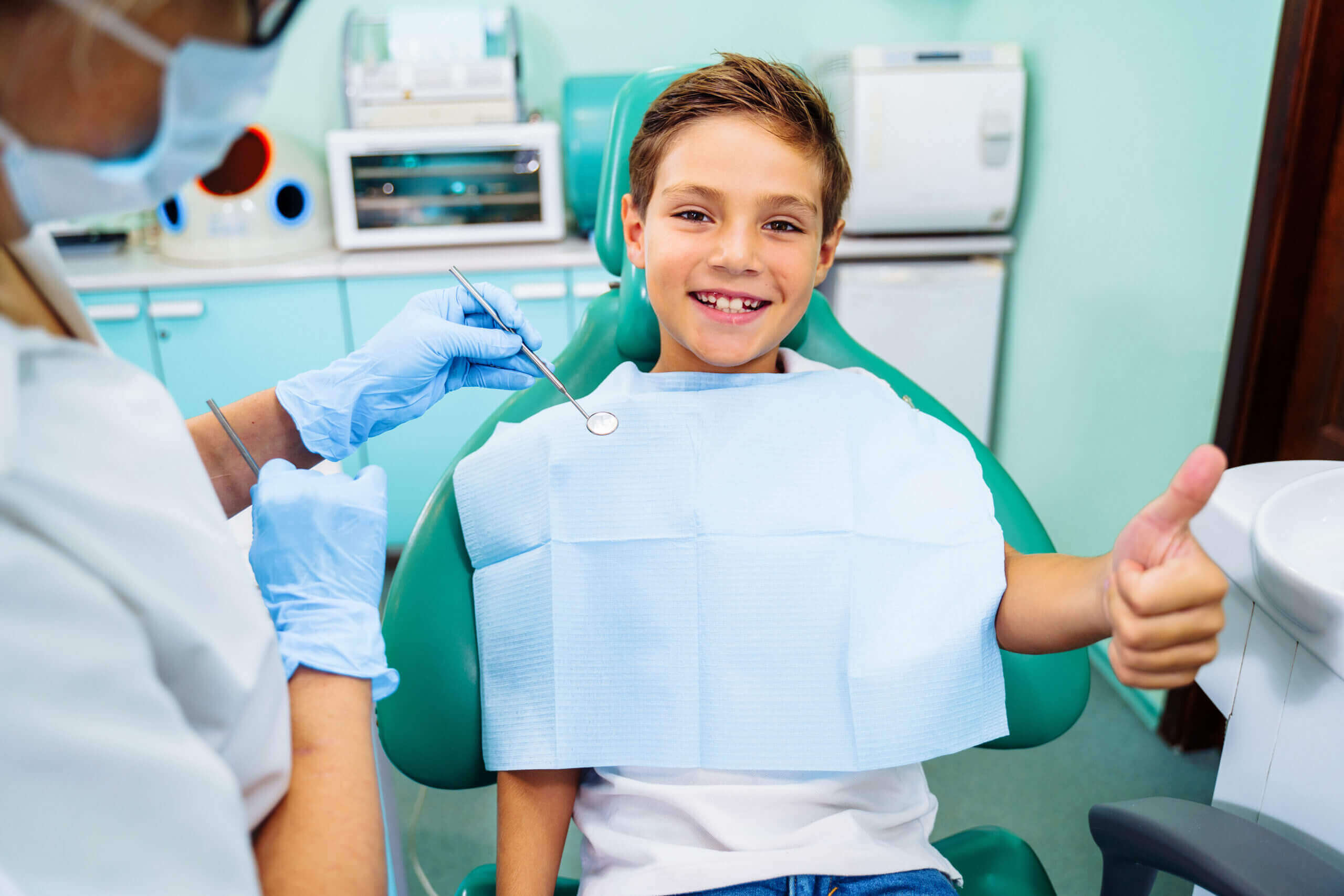 first appointment Small, young patient boy is happy with a visit to the dentist. Concept of painless dental treatment. Beautiful, wide smile of a child sitting in a dental chair in a doctor's office. Thumbs up.