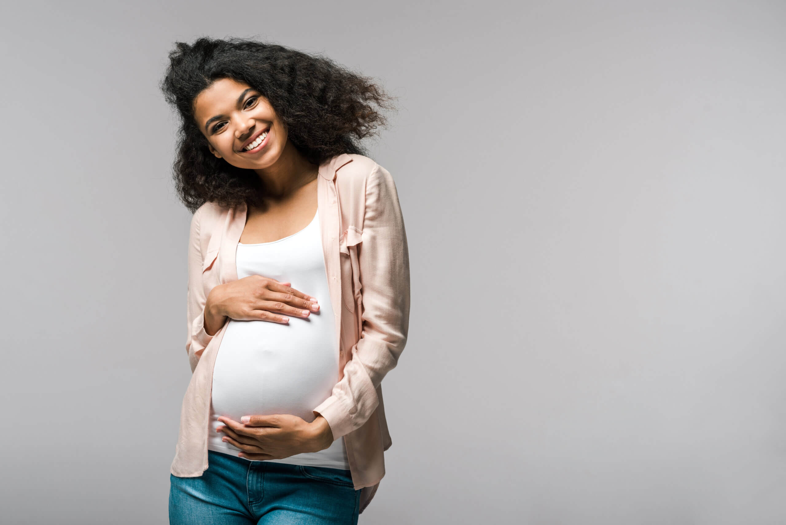 happy young pregnant african american woman touching belly on grey