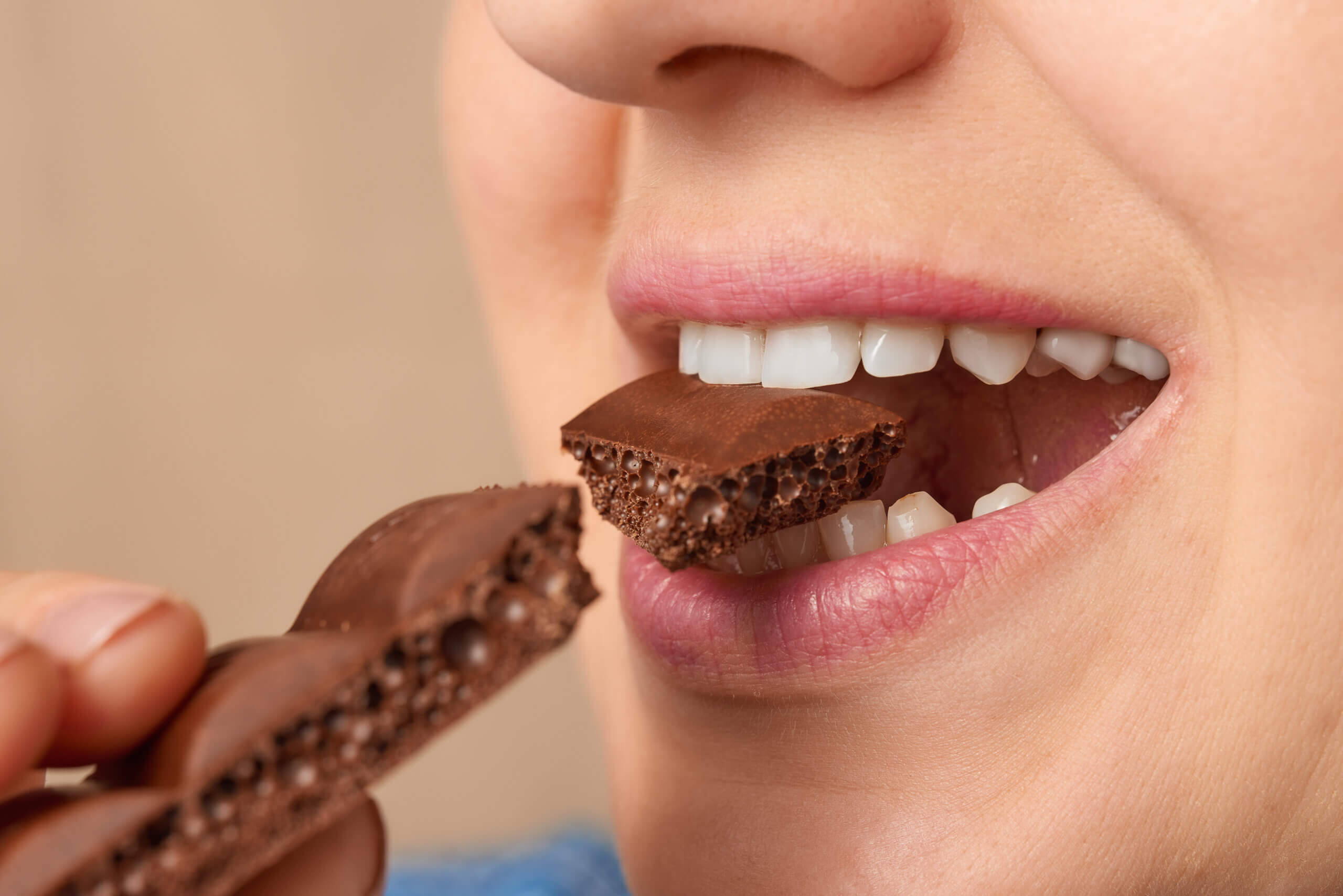 Close up of the mouth of a Caucasian woman biting off a piece of porous chocolate. Three-quarter front view. Low angle view.